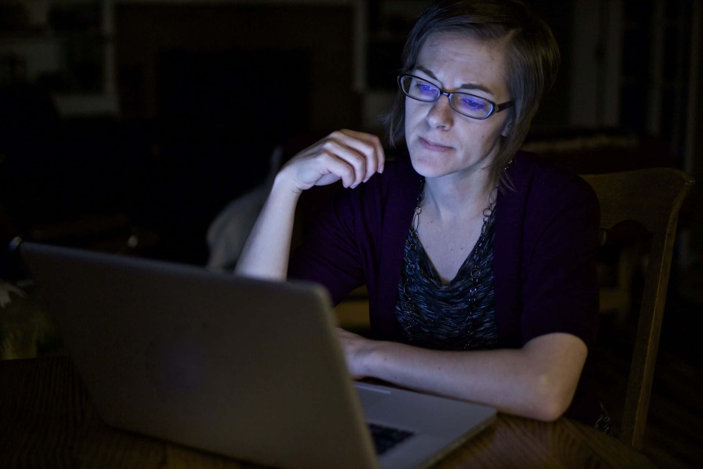 Frustrated woman working on laptop in the dark