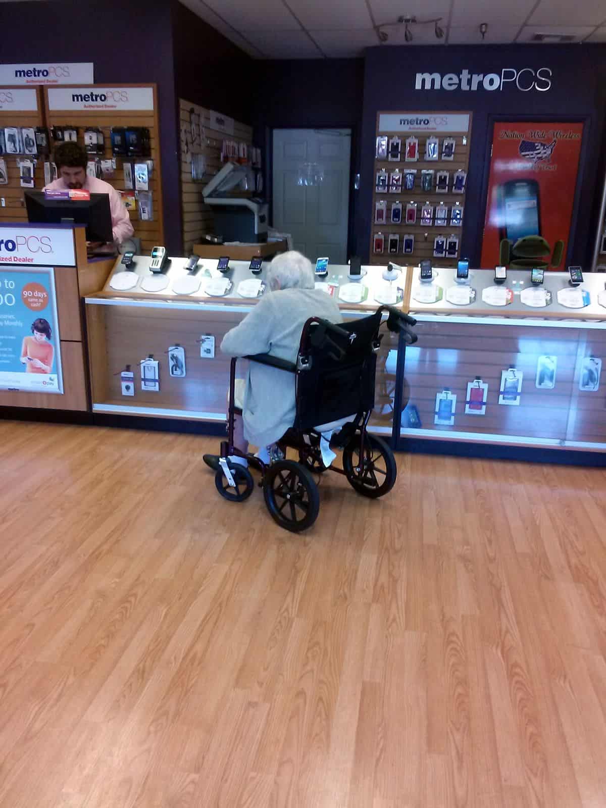 A senior citizen in a wheelchair chooses between several smartphones to purchase.
