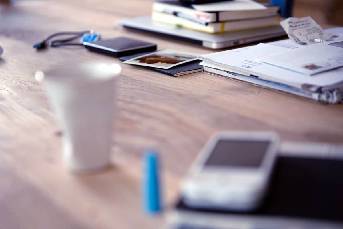 A focused shot of a work desk with a mobile phone out of focus. For designers going from web to mobile app design, there are many things to learn about mobile app UI design.
