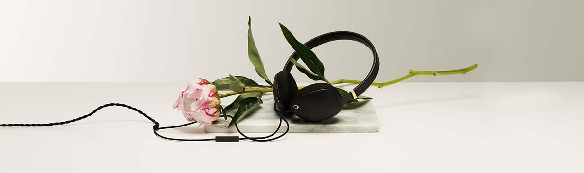 Plica stylish headphones in black laid out next to a pink rose.