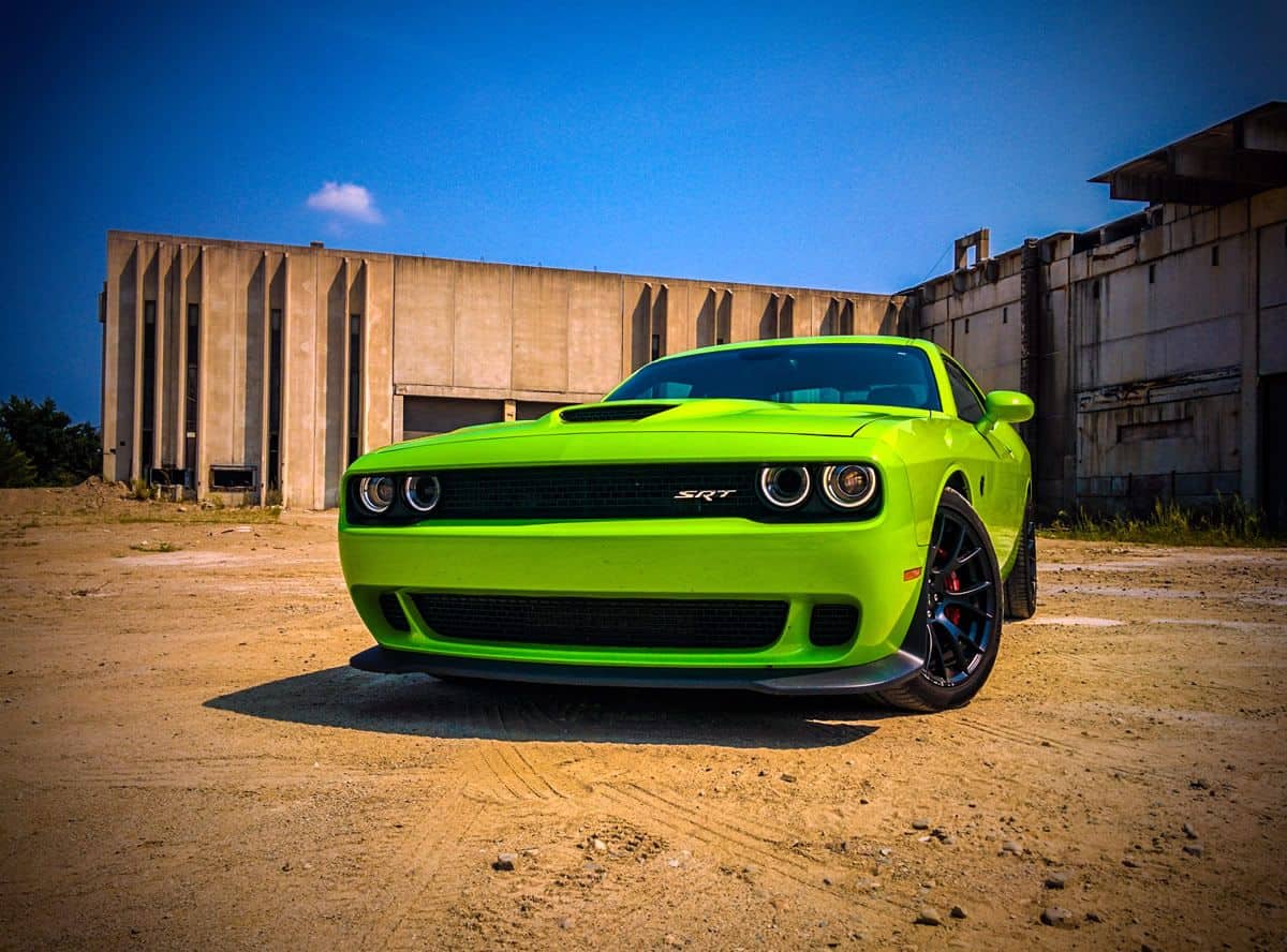 A view from the front of a lime green Dodge Challenger HellCat, parked on a sandy lot.