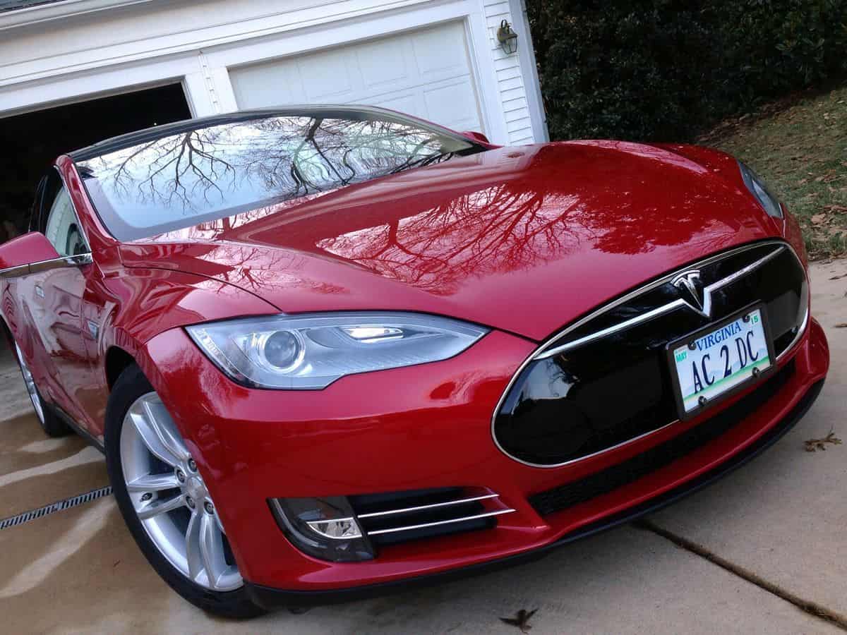 A red Tesla Model S is parked in the driveway in front of a white two-car garage.
