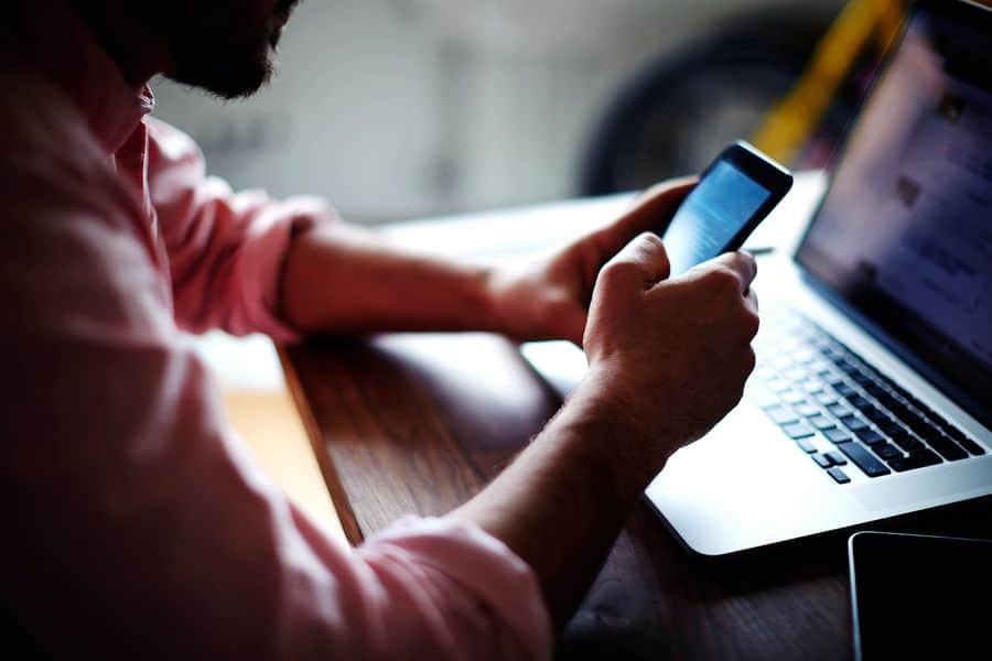 An Android UI designer holds a smartphone in front of his laptop. Using device emulators is an important part of testing Android apps, but it’s still important to get actual devices in your hand to test the UI/UX.