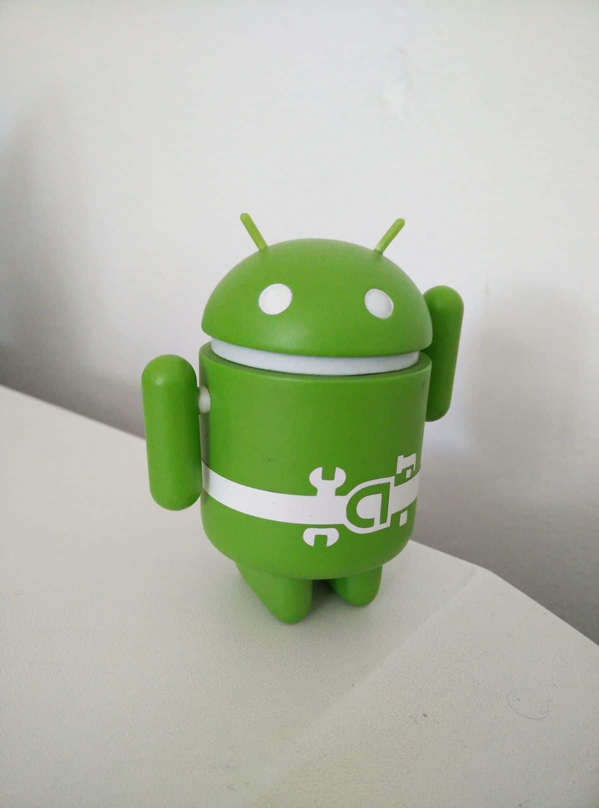 A small, green plastic Android figurine lifts one arm as though waving.