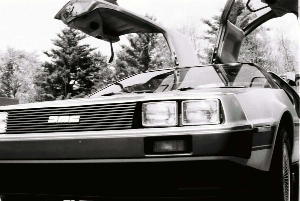 A black and white photo of the front of a DeLorean DMC-12, its characteristic gull-wing doors open.