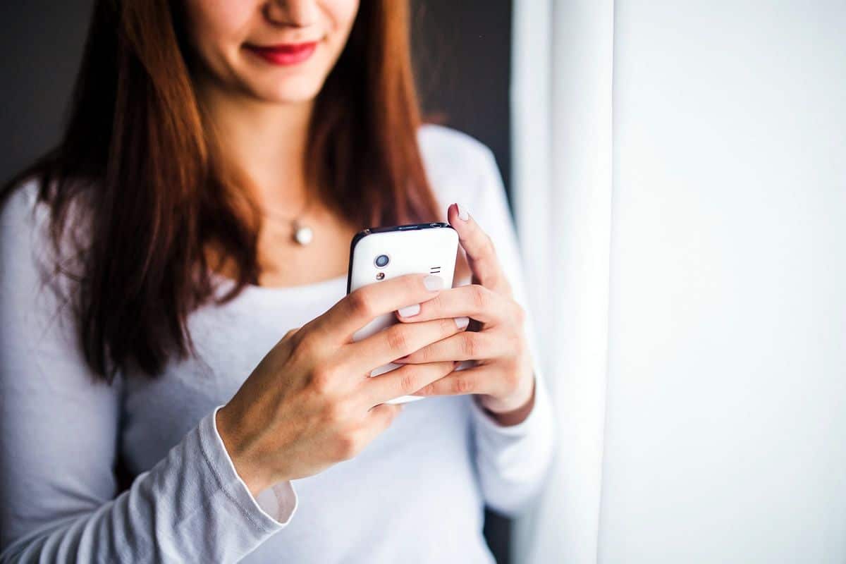 A young woman smiling while looking at mobile phone, which is the kind of reaction guerrilla UXers should aim for