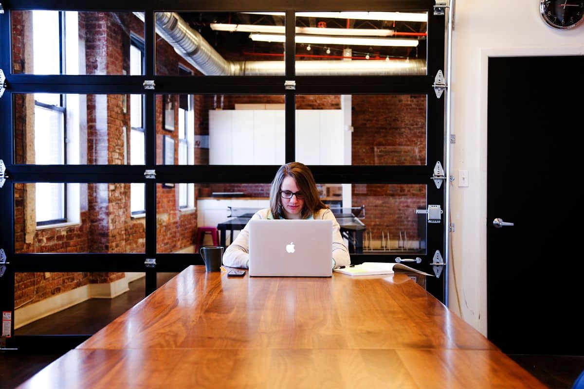 A young woman working on her MacBook at a long table in a stylish office