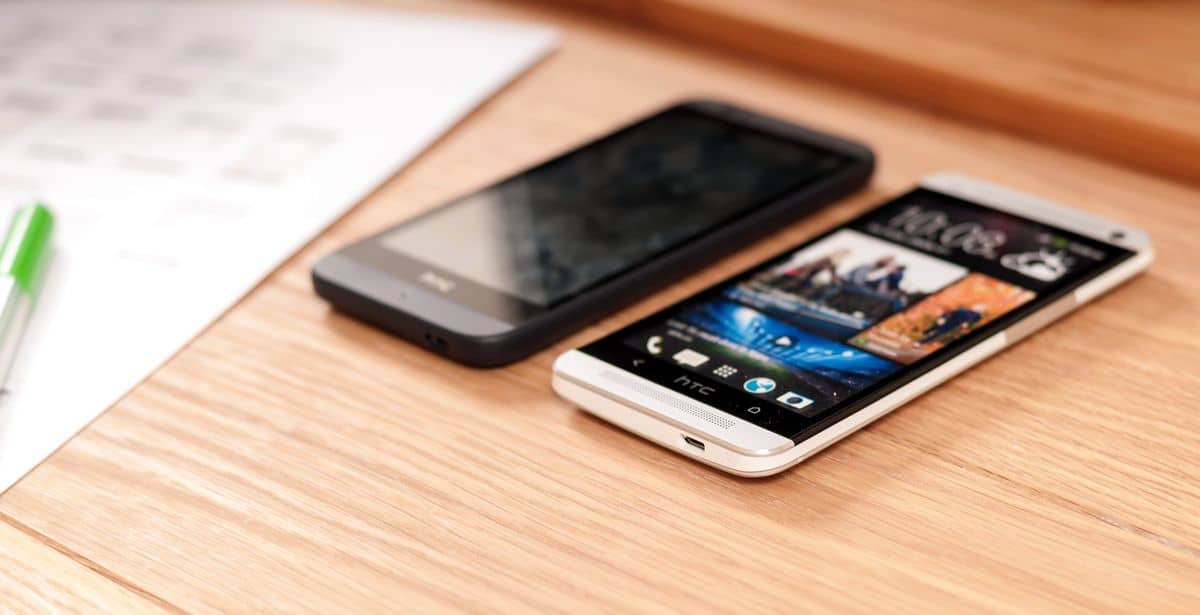 Two HTC mobile phones on a desk and wireframes in the blurred background.