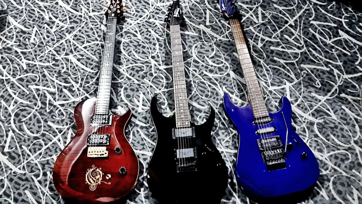 A red Opeth Signature PRS, a black Ibanez, and a blue Squire electric guitar lie next to each other in a row.