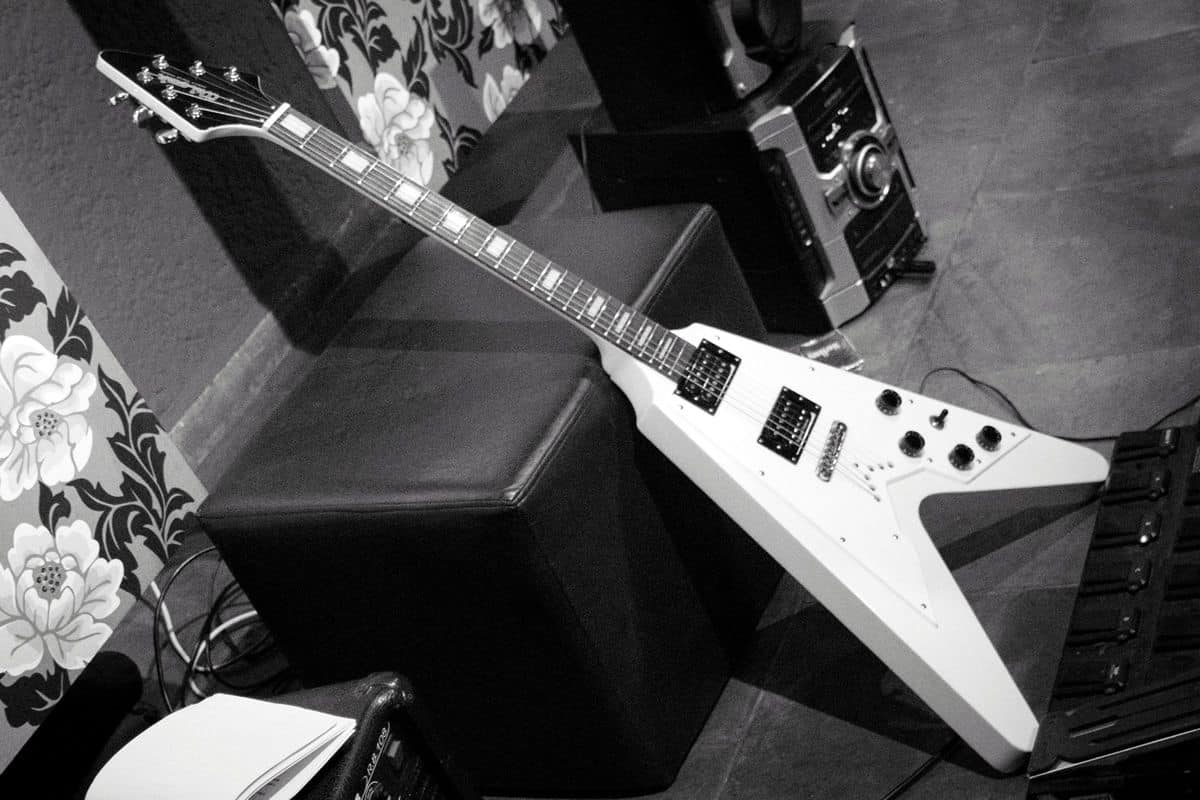 A black-and-white photo of a white Gibson Flying V guitar leaning against an ottoman.