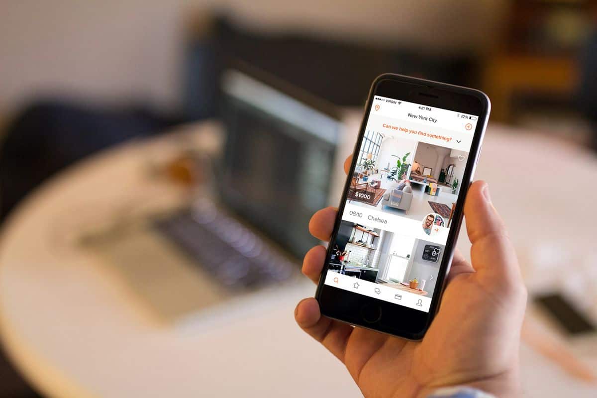 An iPhone displays a screenshot with a picture of a potential apartment on the Roomi iOS app.