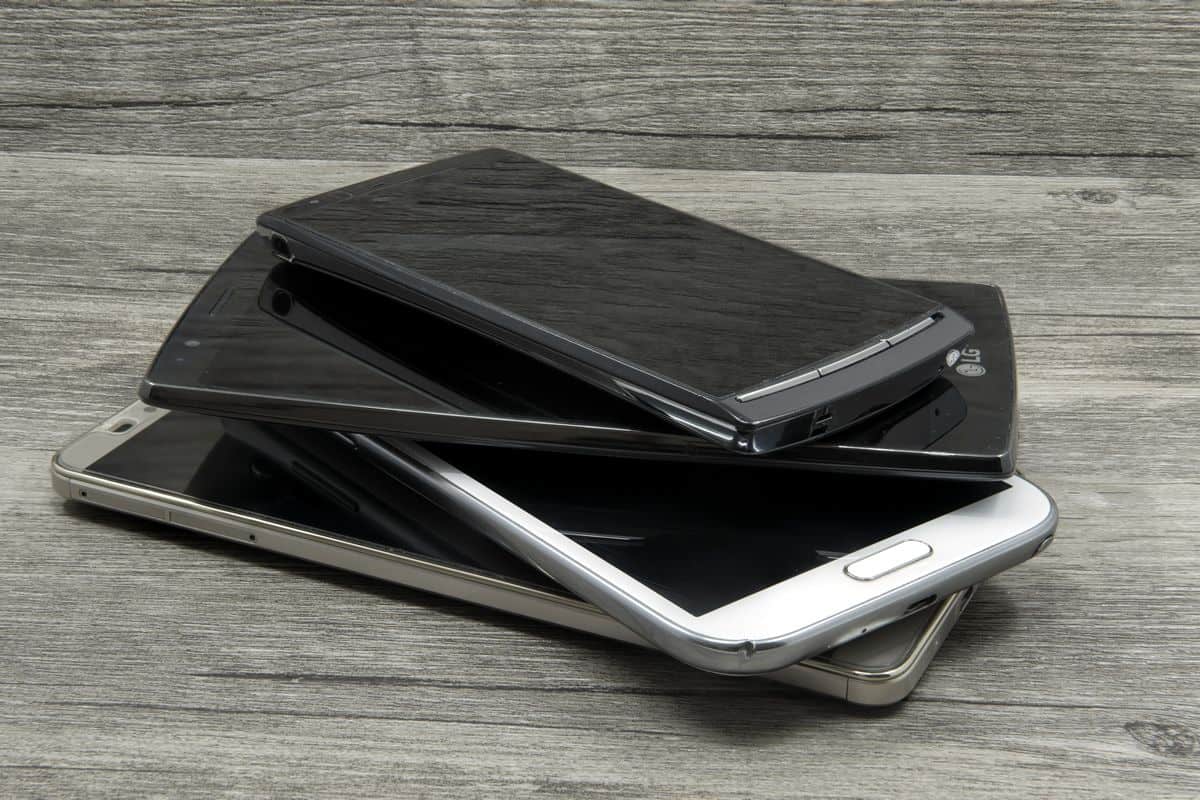 A stack of devices, both iOS and Android, of different sizes and specs sits on a wood table, ready for testing.