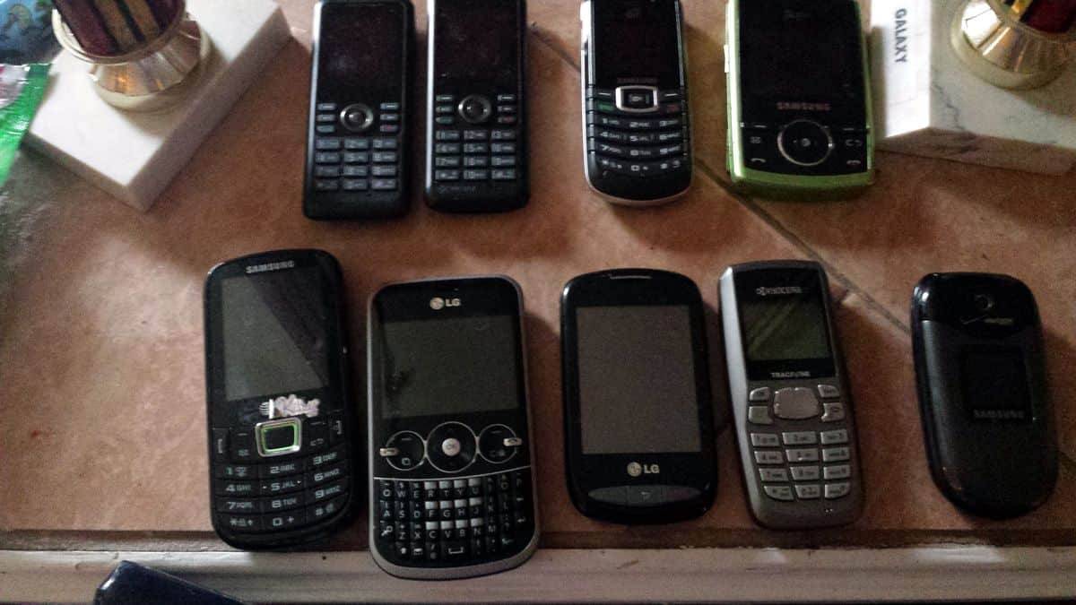 Nine outdated cell phones, a mix of smartphones and feature phones, lie flat on a desk.