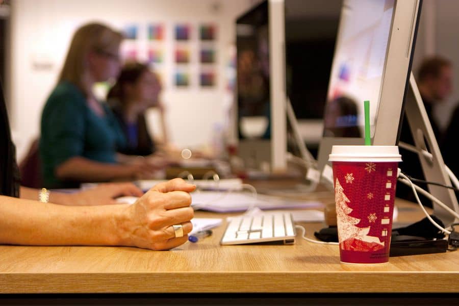 Multiple designers at a graphic design business sit in an open office in front of iMacs. A cup of Starbucks coffee sits in the foreground.