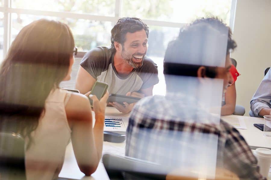 The view from outside an office window of a group of young designers having a business meeting gathered around the table with their mobile devices.