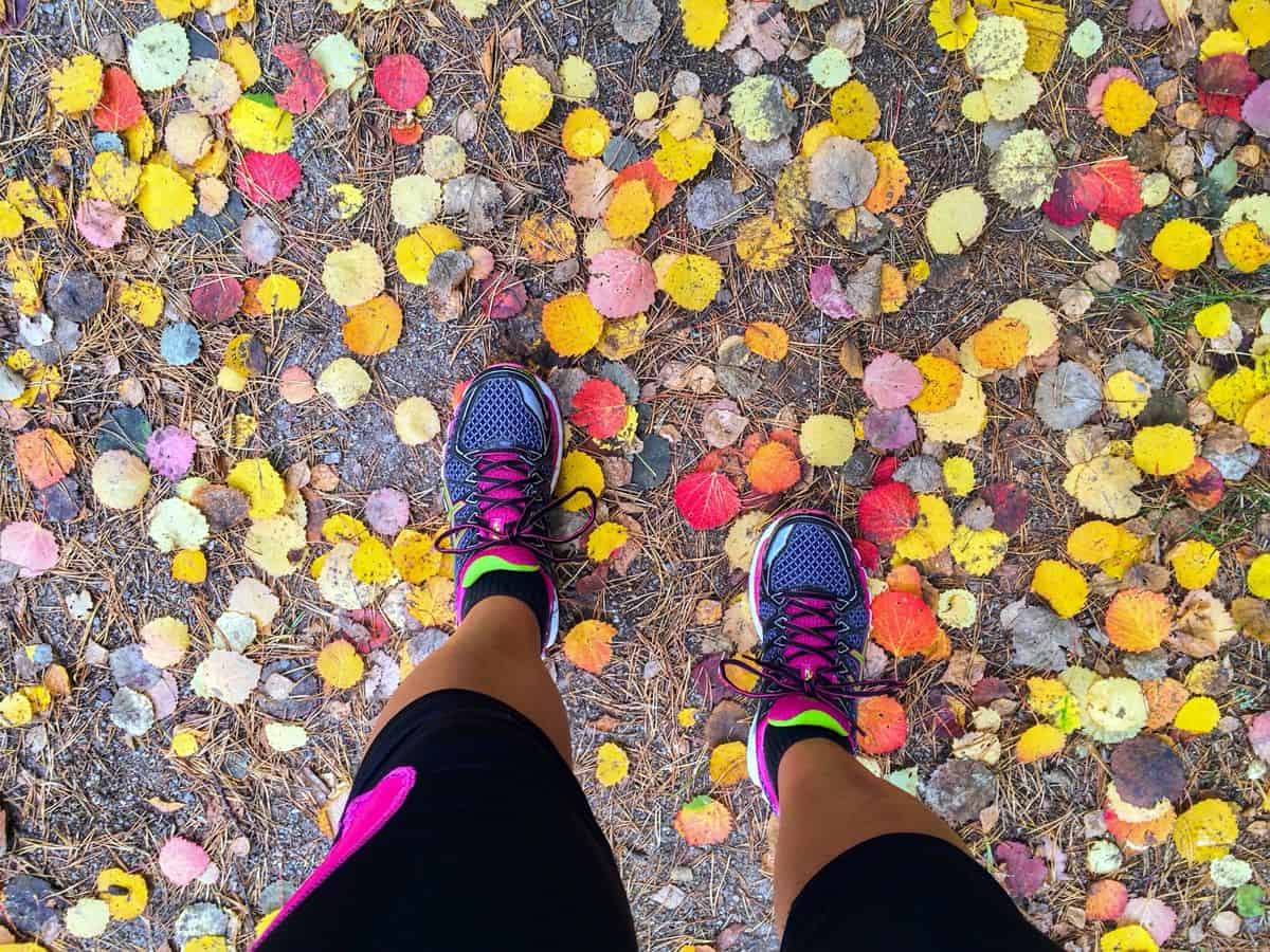 A top-down view of a woman wearing brightly colored running sneakers on a fall day, with leaves on the ground around her.