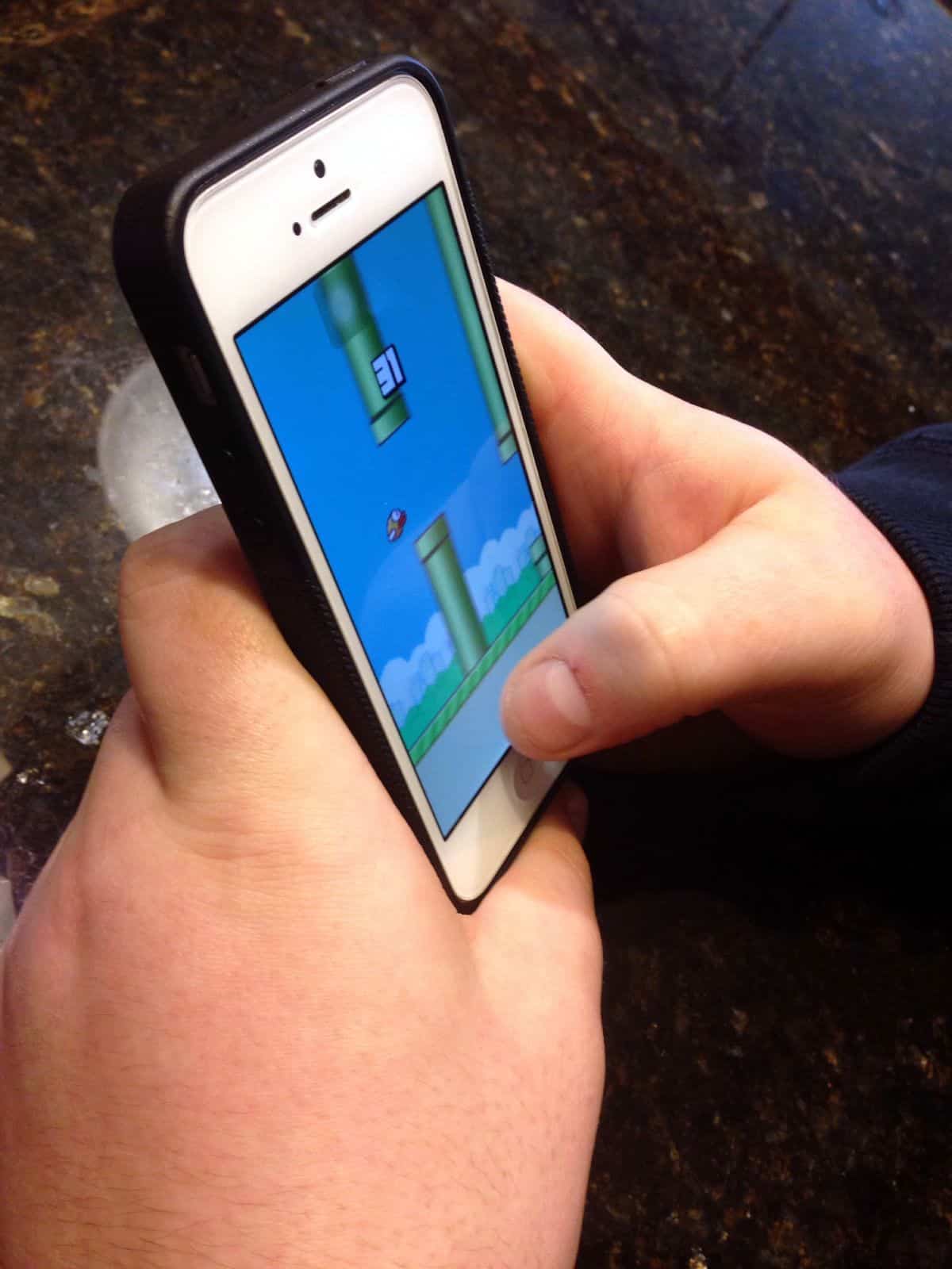 A close-up of a person playing Flappy Bird, a game as challenging as it is addictive, on an iPhone.