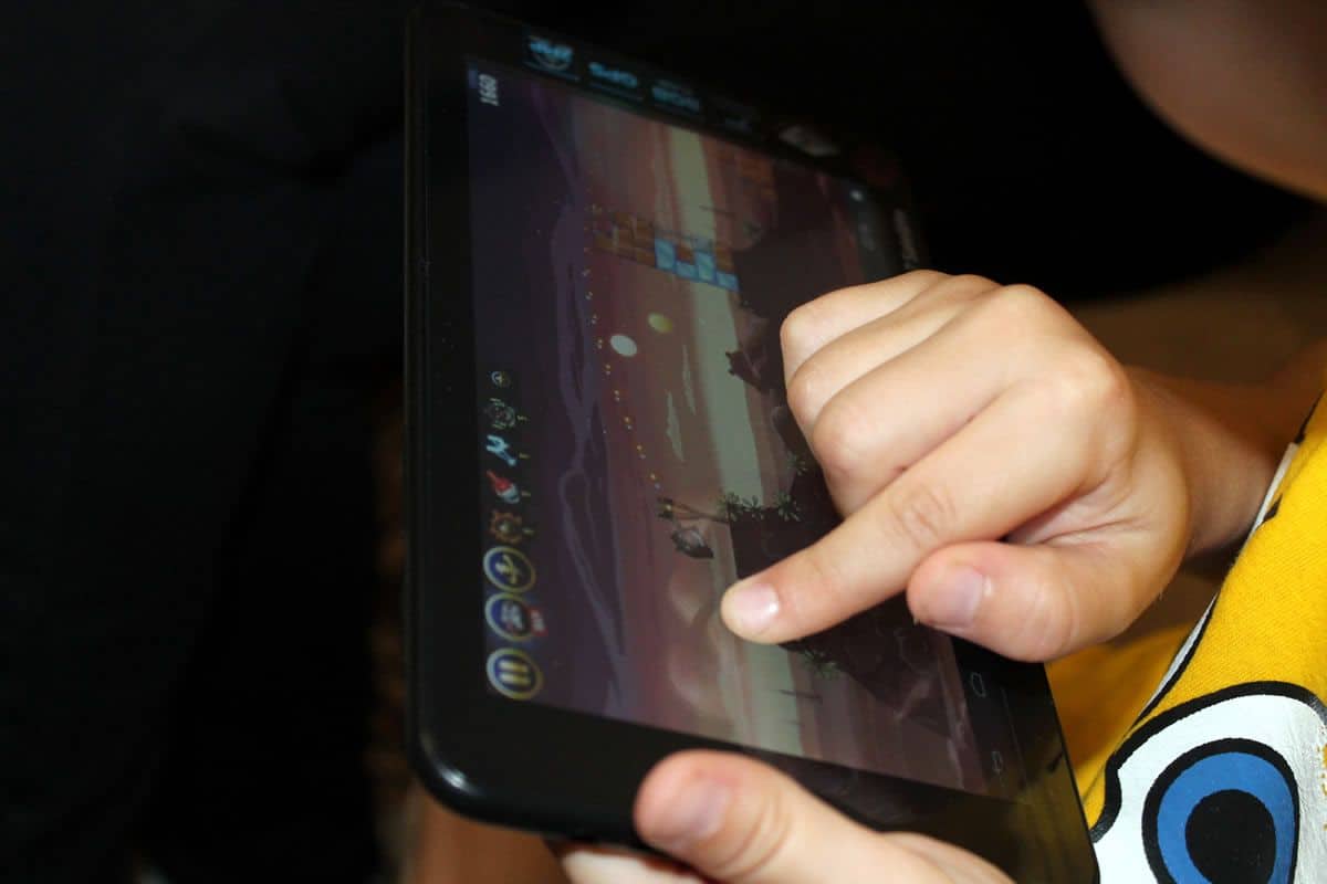 A close-up of a child’s hand playing Angry Birds on a tablet.