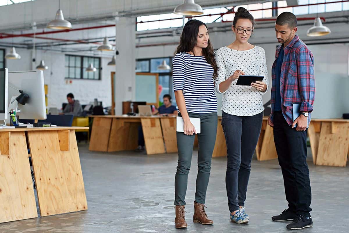 Three UX visual designers holding tablets gather around a single tablet to look at a design.