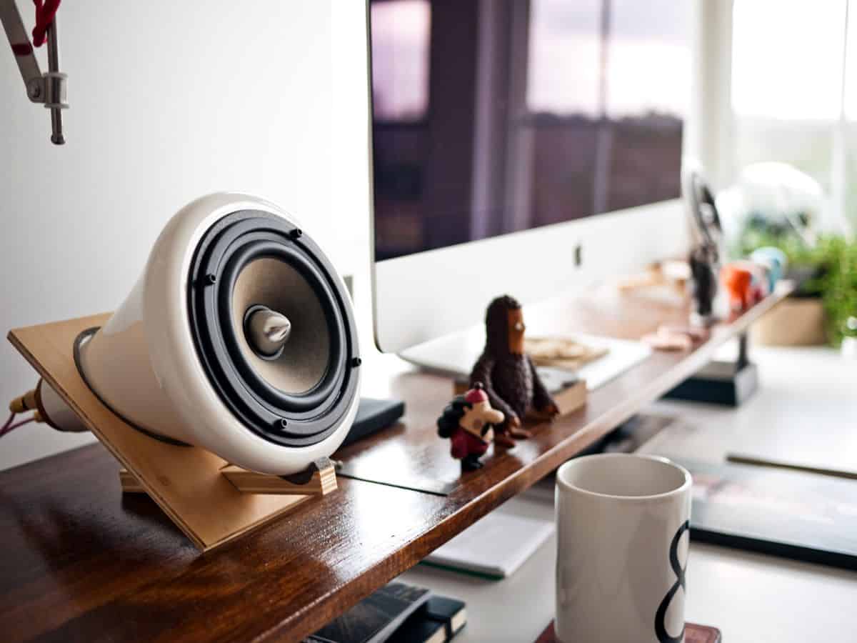 A close-up photograph of a set of audio speakers connected to an Apple iMac display on a designer desk setting.