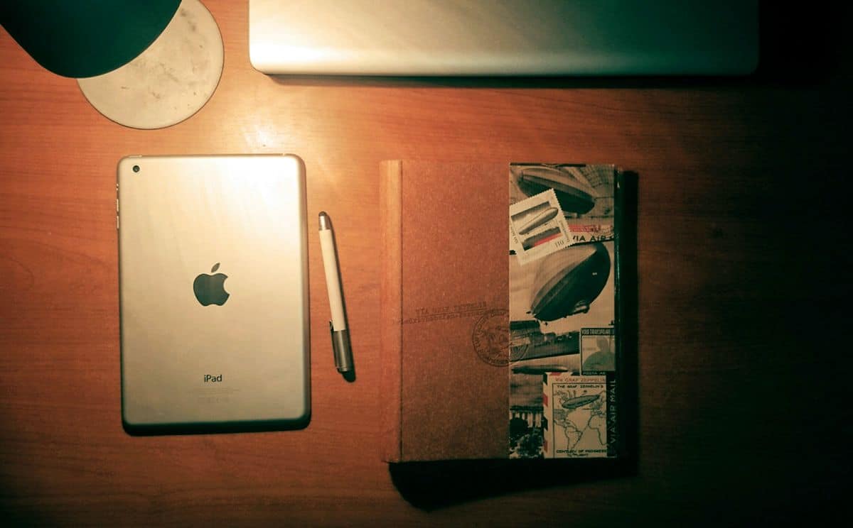 A photo of a designer’s desk with an iPad, stylus, sketchbook and MacBook.