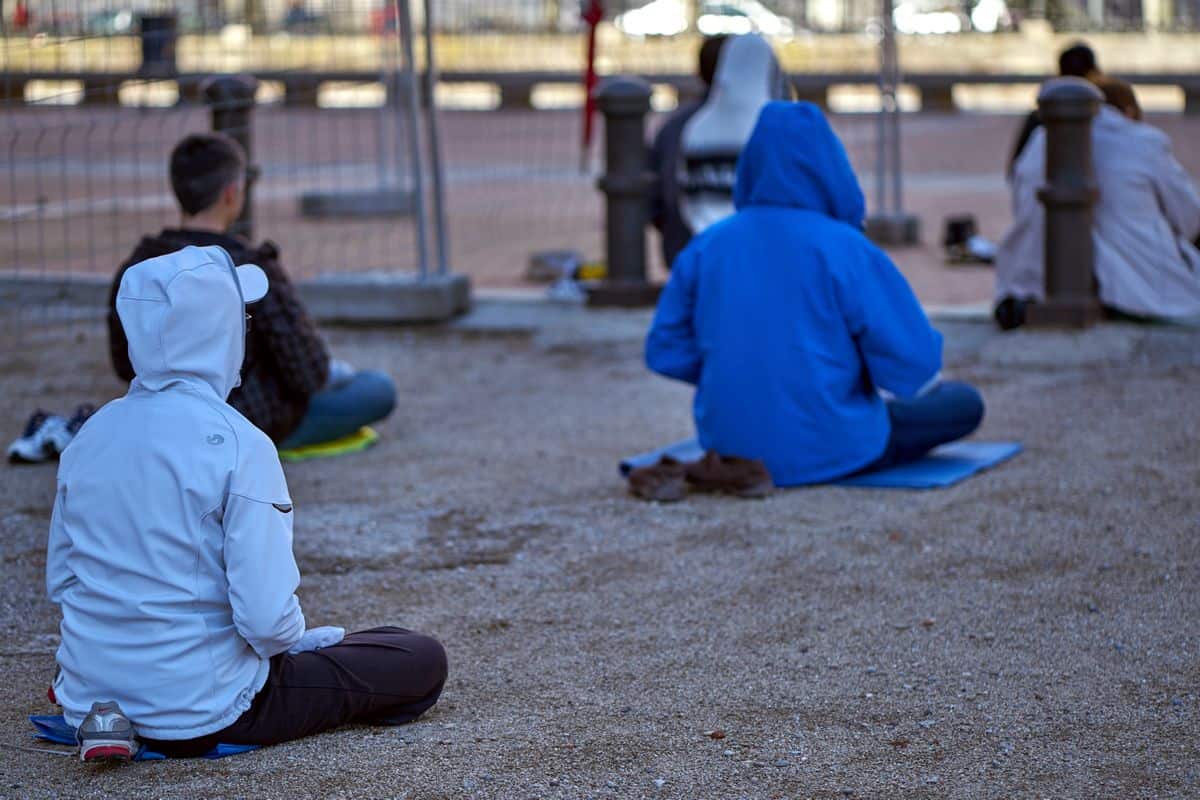 A number of students sit cross-legged in a park, practicing mindfulness meditation.