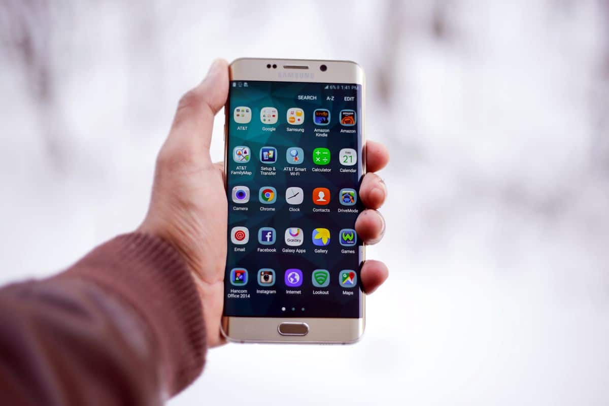 A man holds a large Android smartphone displaying 25 app icons on the home screen grid.