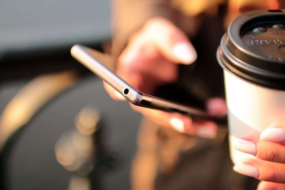 Close up of a mobile user with a phone in one hand and a takeaway coffee cup in another. Letting users show you how they use their devices during user interviews can be very helpful.