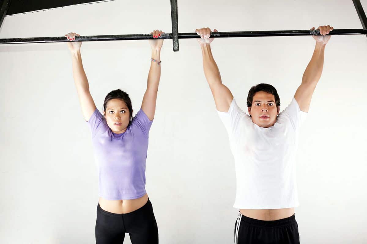 Two personal trainers, one male and one female, hang from a large pull-up bar. Thanks to mobile app visual designers, your smartphone can bring the personal trainers to you.
