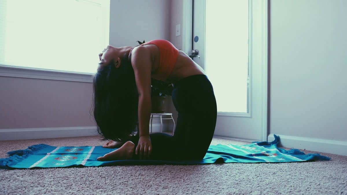 A woman in camel pose practices yoga in her own home, a possibility made easier by visual designers creating apps for personal fitness.