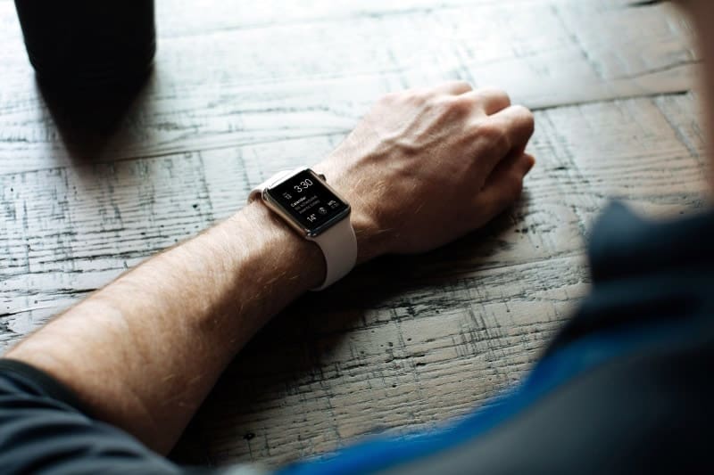 Close up image of the Apple Watch white band on a male user’s arm resting on a wooden table.