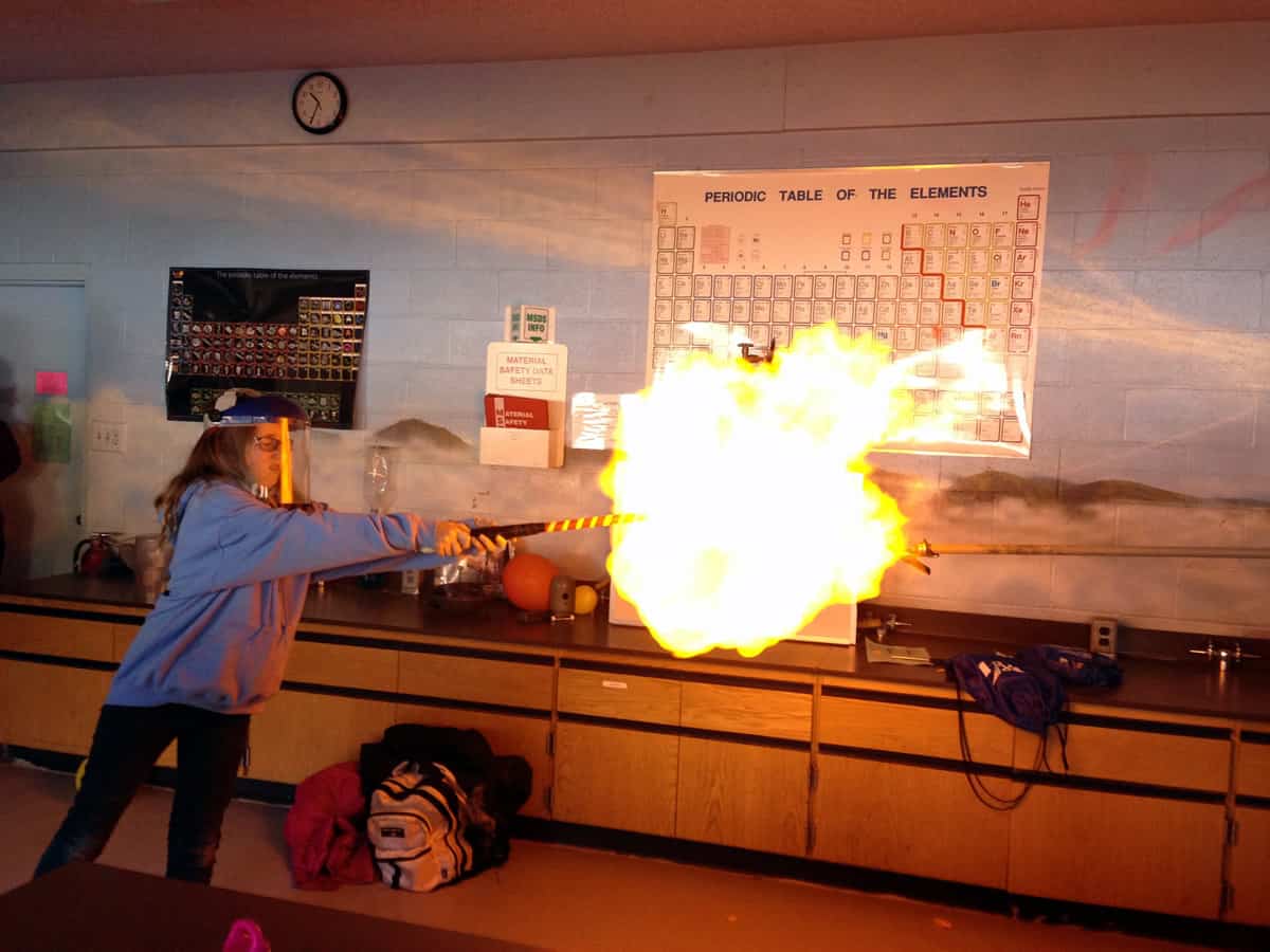 A chemistry major wearing ample safety gear creates a makeshift blowtorch in a college classroom.