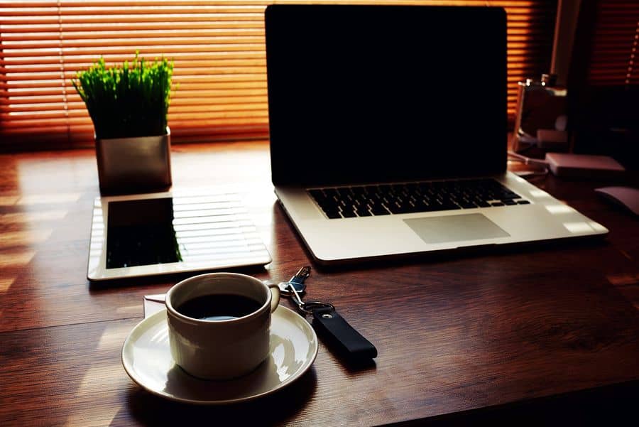 An iPad, MacBook and cup of coffee sit neatly on a wooden desk. These tools and an Internet connection are all you need to learn how to design apps online.