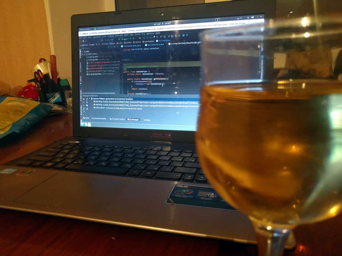 A photo of a glass of wine in front of a laptop displaying a screen from Android Studio.