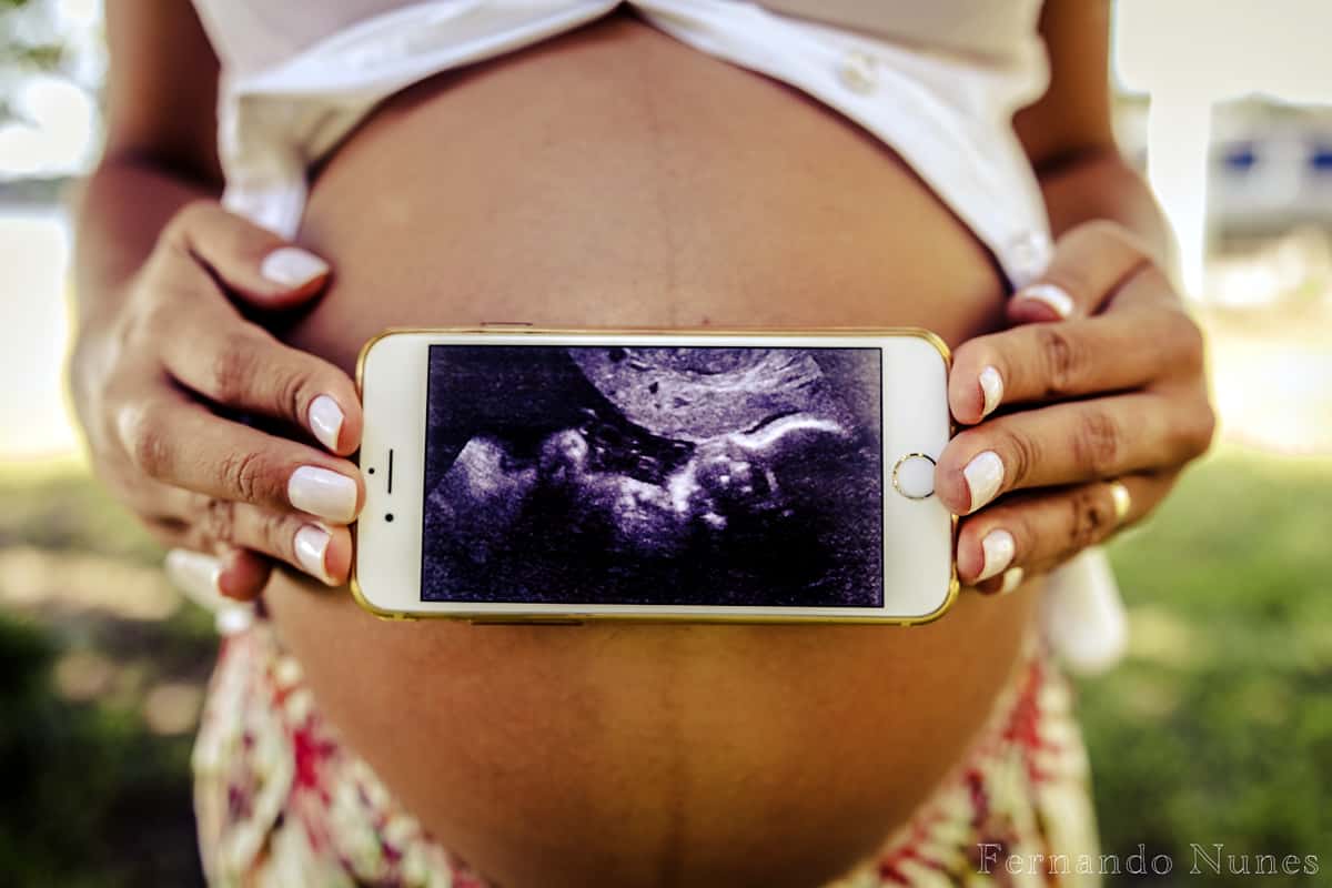 A pregnant woman holds an iPhone with a photo of her ultrasound in front of her stomach.