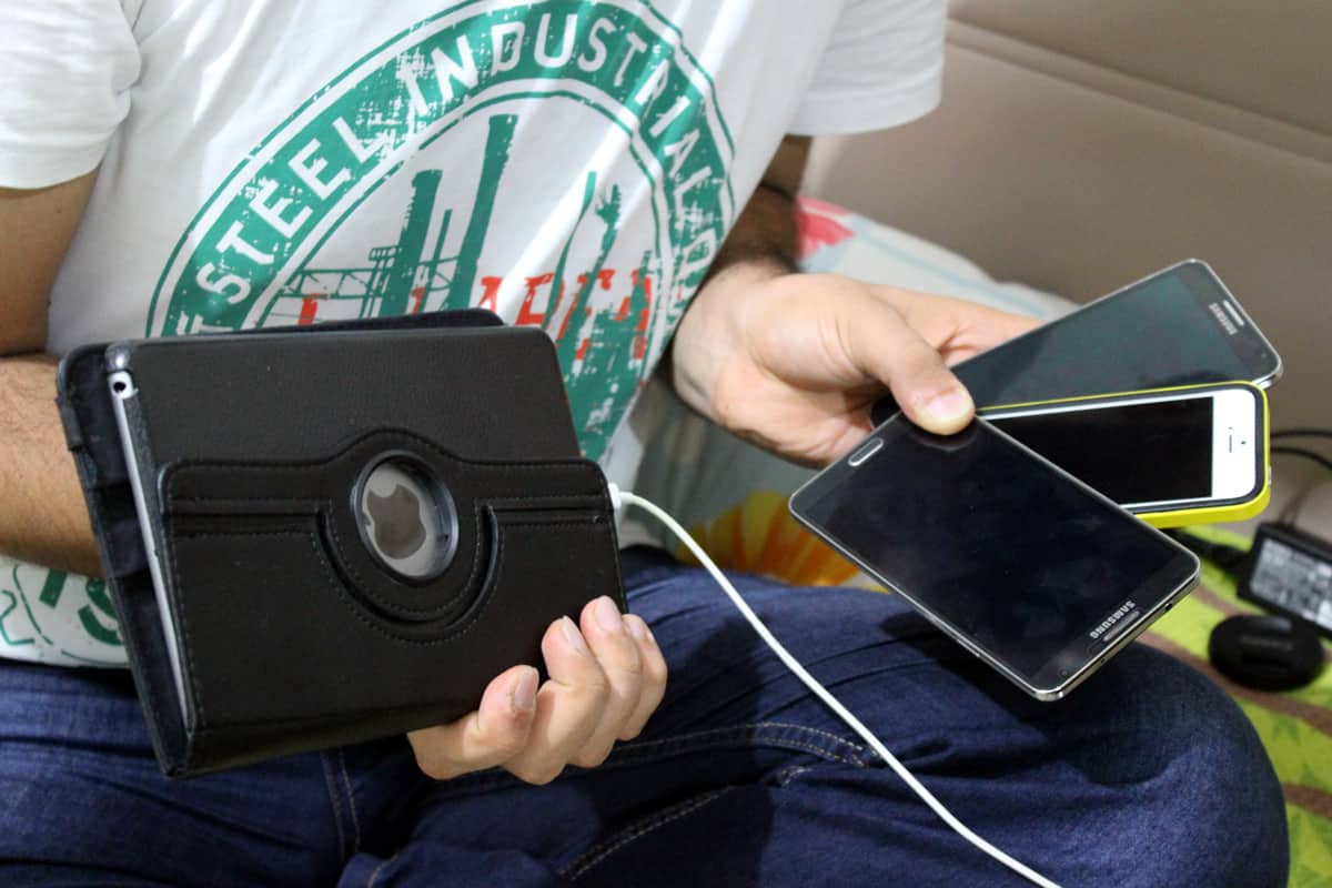 A man holds three smartphones in one hand and an iPad in the other.