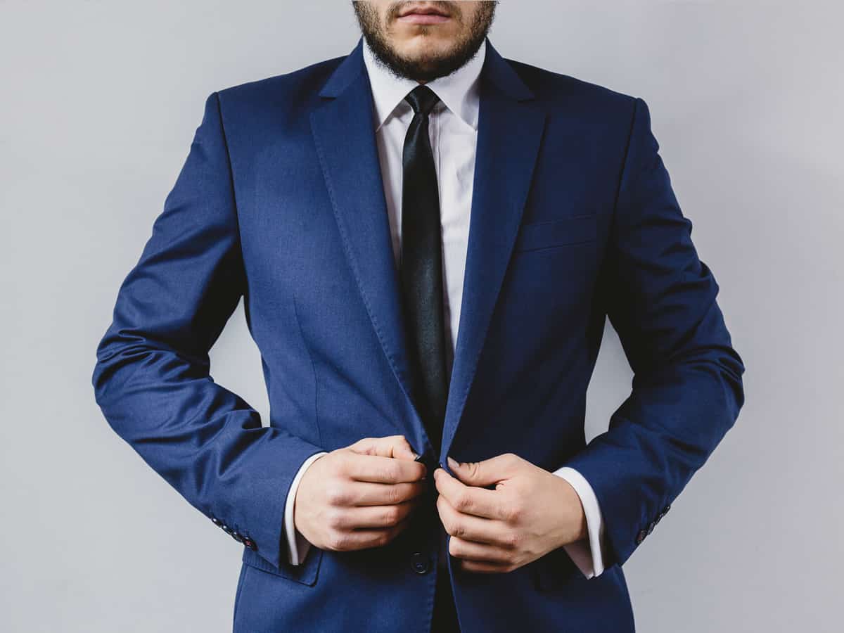 Close-up view of a man in a smart well-tailored blue suit standing upright about to button up his blazer.