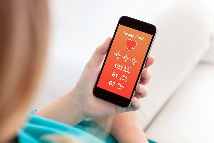A woman holds a smartphone showing a fitness app displaying blood pressure and pulse rate.