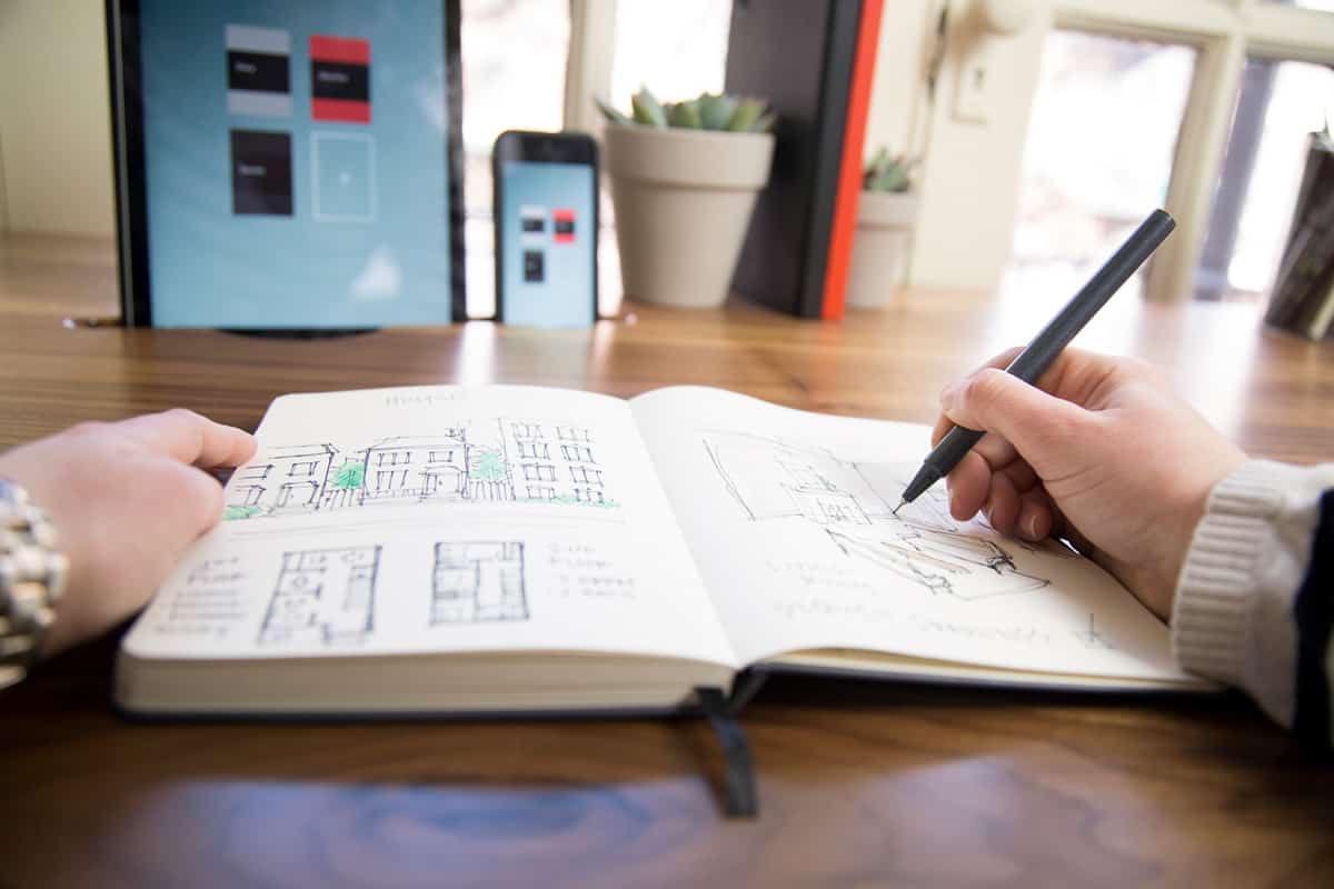 A person sketching on the Mod Notebook with and iPhone and iPad in the background showing digitized copies of other notebook contents.