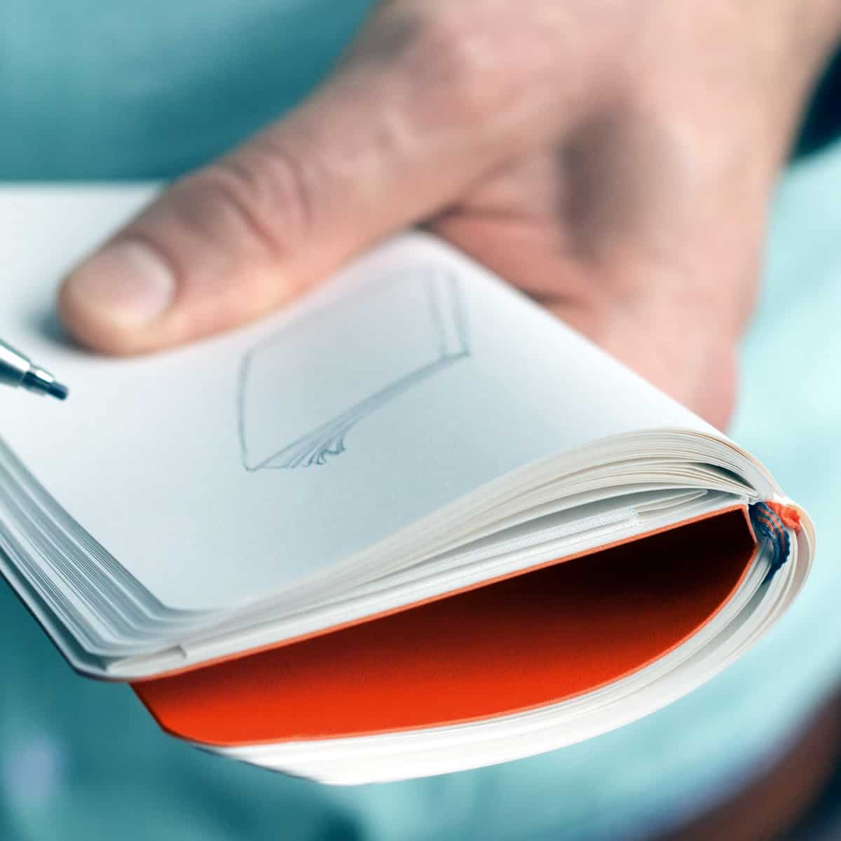 Close-up of a hand holding an opened Notebook Pocket A6 with a drawing of a notebook on the page.