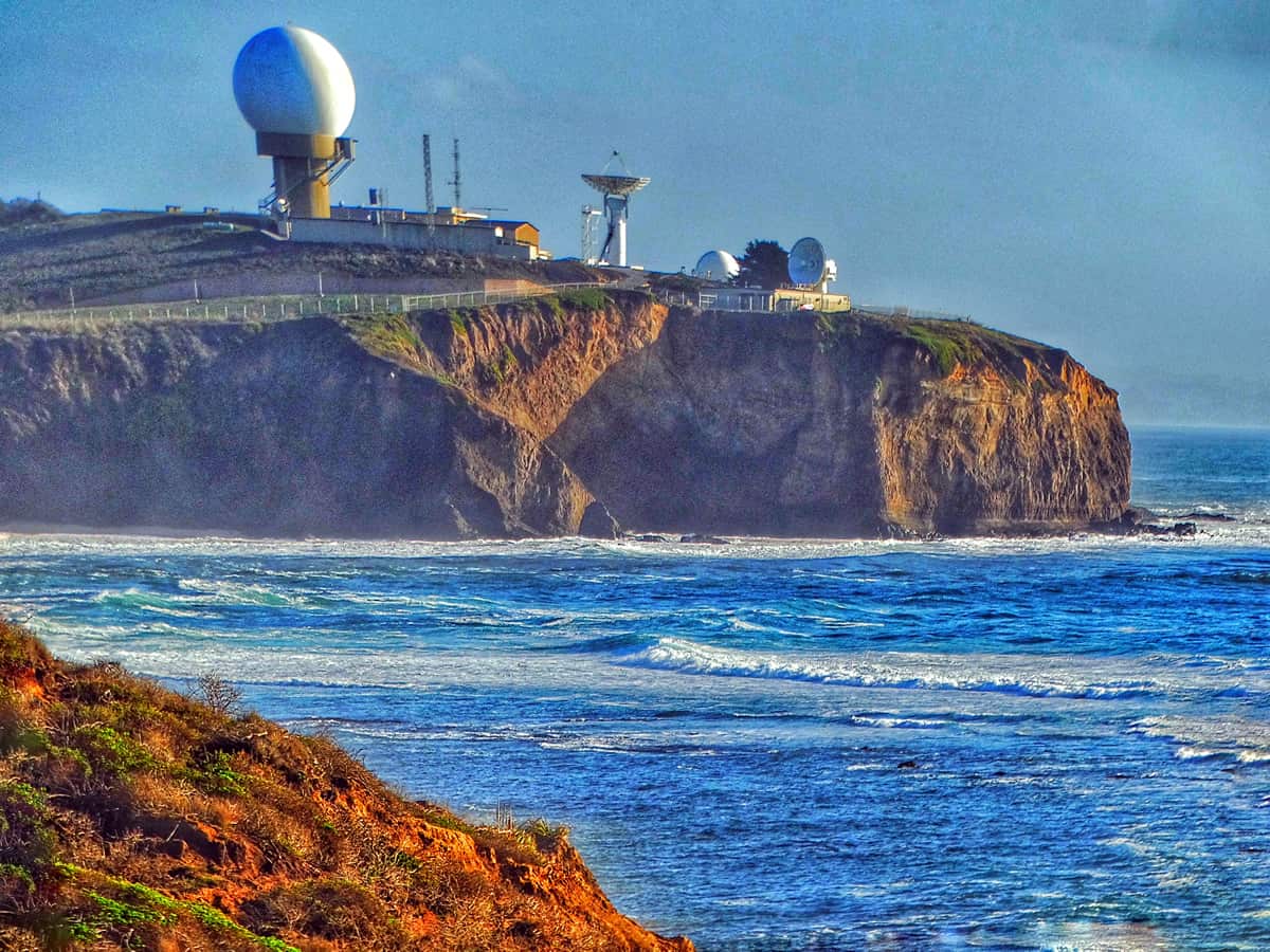 A picture of a US military installation on top of a cliff overlooking a beautiful blue body of water. DARPA helped shape many technological advances we take for granted today, like wearable technology and the Internet itself.