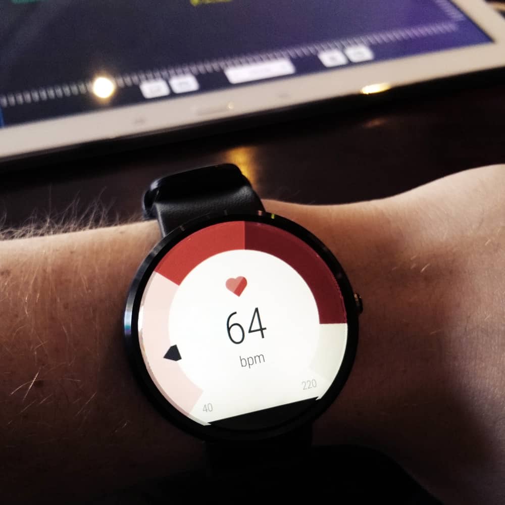 A close-up photo of an Android Wear watch displaying a heart rate of 64 BPM.