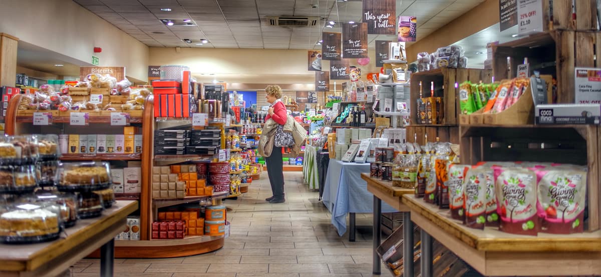 A photo of a woman standing in the aisles of a grocery store.