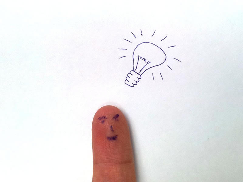 A photo of a finger with a happy face on it with a light bulb drawing in the background.