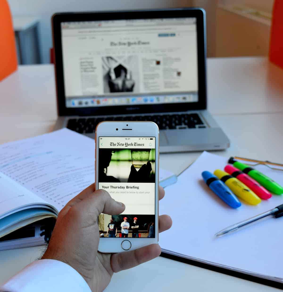 A photo of a man scrolling through his iPhone while sitting at his desk.