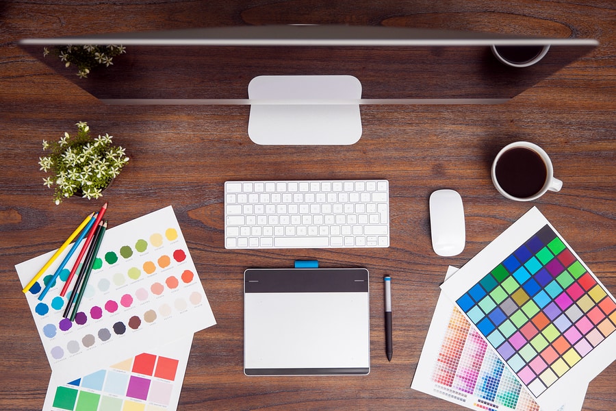 A photo of someone’s desk, complete with computer, color charts, drawing tablet, and coffee.