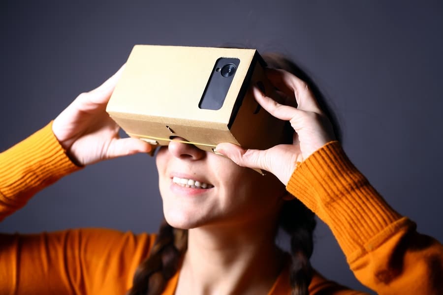 A photo of a smiling woman holding Google Cardboard up to her eyes.