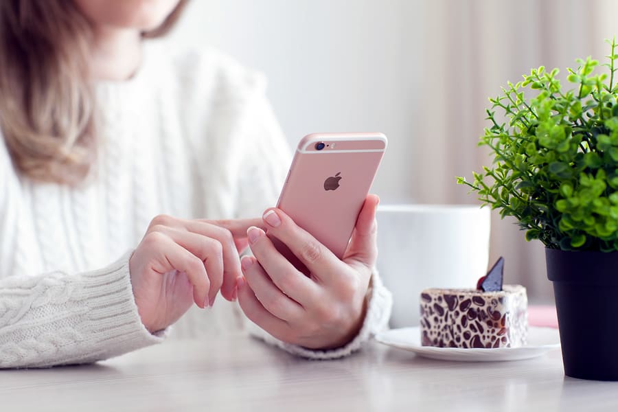A photo of a woman sitting in a cafe holding a rose gold iPhone, undoubtedly playing with some of our coolest apps.