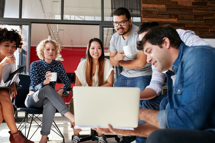 A photo of a group of people looking at a laptop screen during a meeting.