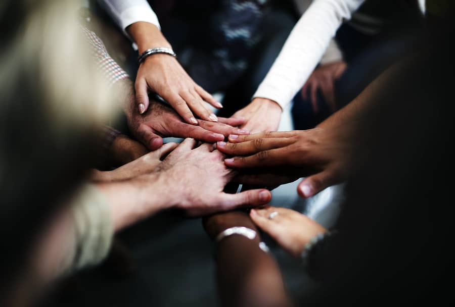 A photo of many hands put into a circle in a show of team unity.